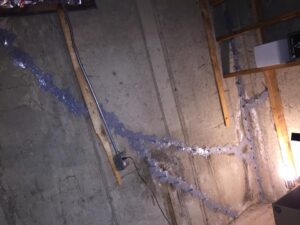 Concrete basement wall with large cracks filled and sealed using a grey epoxy sealant during a premium waterproofing repair.