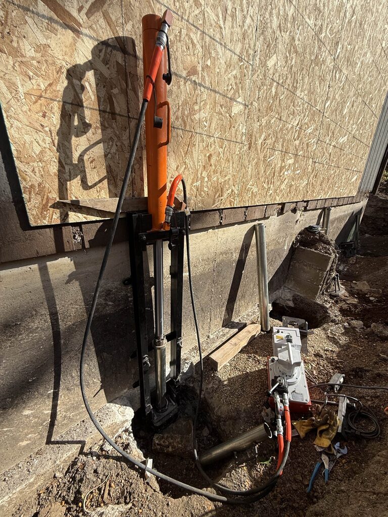 Hydraulic foundation pier driving system installed beneath an exposed concrete footing to lift and stabilize a settling structure.