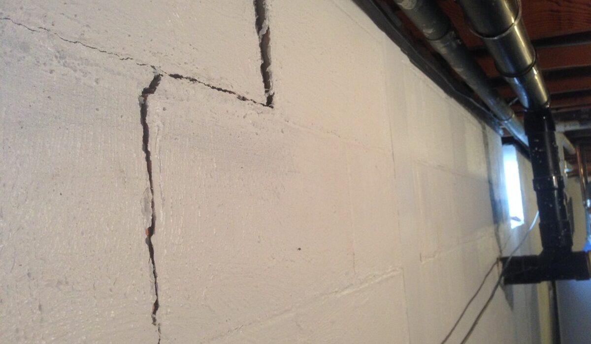 Cracked cinder block basement wall showing structural damage caused by failed DIY wall reinforcement methods.
